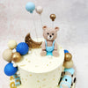 The centrepiece of this Nursery Theme Cake features an adorable textured teddy bear wearing powder blue dungarees, perfectly poised atop a cream-coloured canvas dotted with shimmering golden flakes. 