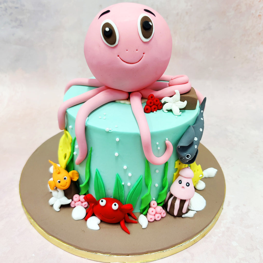 At the centre of this Octopus Theme Cake is the charming pink octopus, with its oversized, expressive eyes and welcoming smile, as if inviting you to explore the ocean floor. 