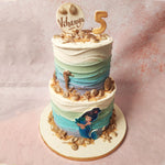 Each layer of this Mermaid Two Tier Cake is artfully adorned with a gradient of purple, blue, green, and cream white hues, meticulously frosted in velvety buttercream to mimic the gentle caress of ocean waves.