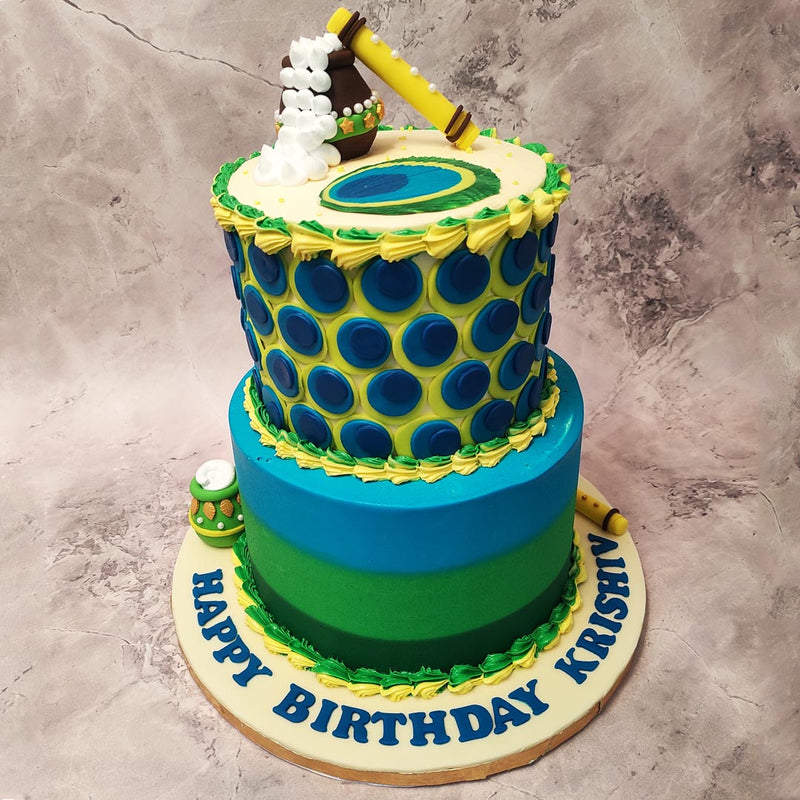 As you gaze upon this peacock Krishna cake, you will be captivated by its enchanting design. The bottom tier of this Janmashtami cake design showcases three layers in shades of dark green, light green, and blue, representing the lush forests where Lord Krishna spent his childhood. 