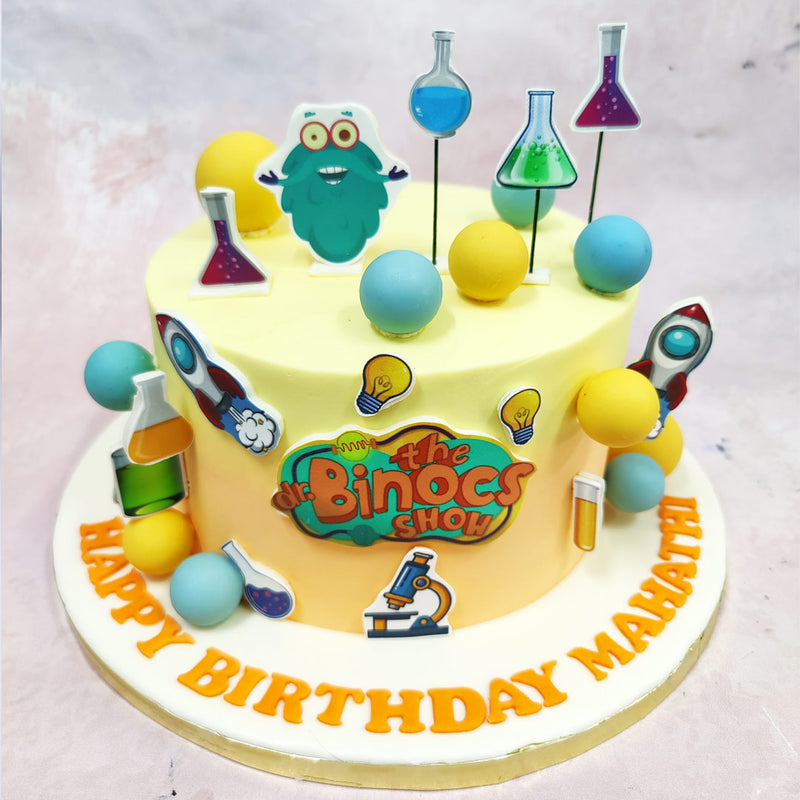 The highlight of this Peekaboo Cake is the bold edible cut-out of Dr. Binocs himself, perched with wide-eyed excitement among a forest of bubbling beakers and test tubes. From vibrant green potions to bright blue flasks, each topper captures the whimsy and wonder of at-home experiments and animated learning.