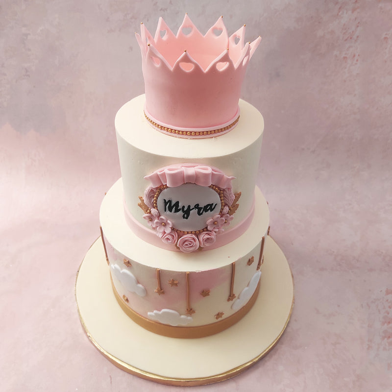 The bottom tier of this pink crown cake is truly mesmerising, featuring fluffy white clouds and hanging gold stars.