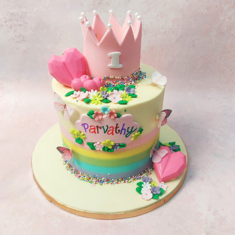 At the heart of this Pink Crown Cake lies: a majestic pink crown adorned with edible white pearls, complimented by 2 pink heart-shaped piñata elements.