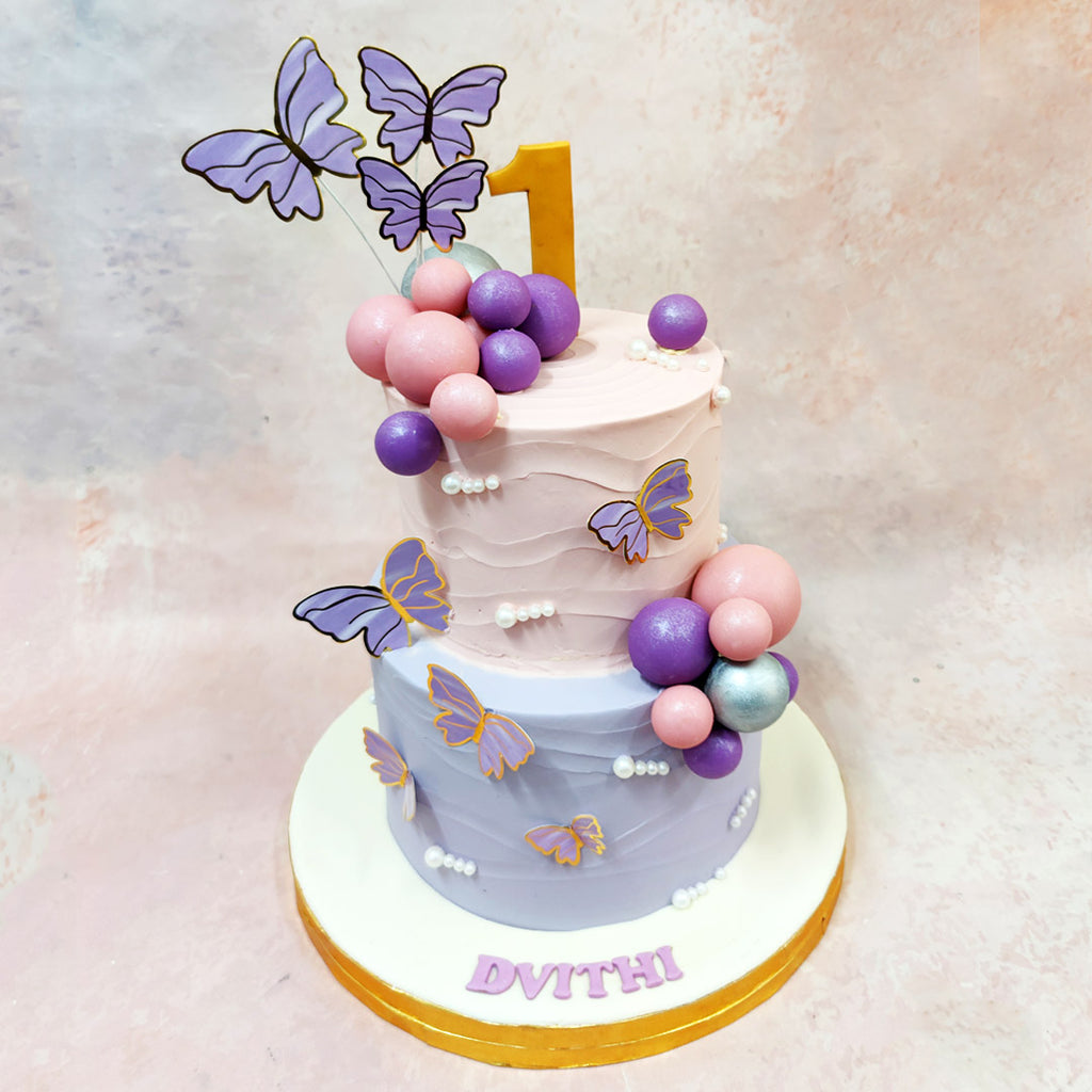 Two-tier birthday cake with butterflies and balloons on a light background