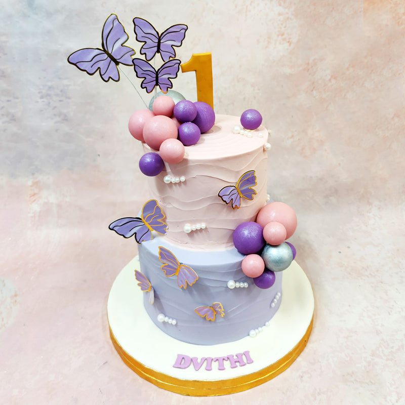 Two-tier birthday cake with butterflies and balloons on a light background