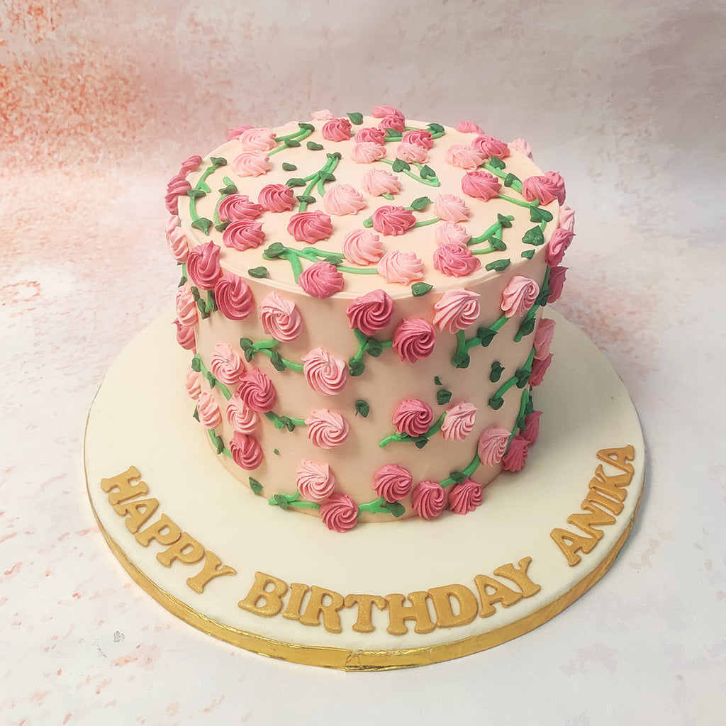 The meticulous piping of the flowers and the addition of green leaves create a vibrant and whimsical effect, capturing the essence of a blooming rose garden on this Pink Floral Cake. 