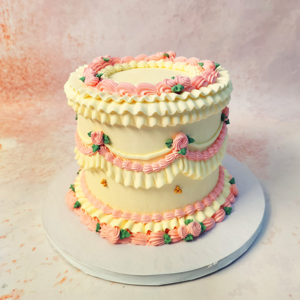 This Pink and White Vintage Cake features exquisite piped details, with intricate ruffles and rosettes adorning each tier, creating a visually stunning and romantic design.