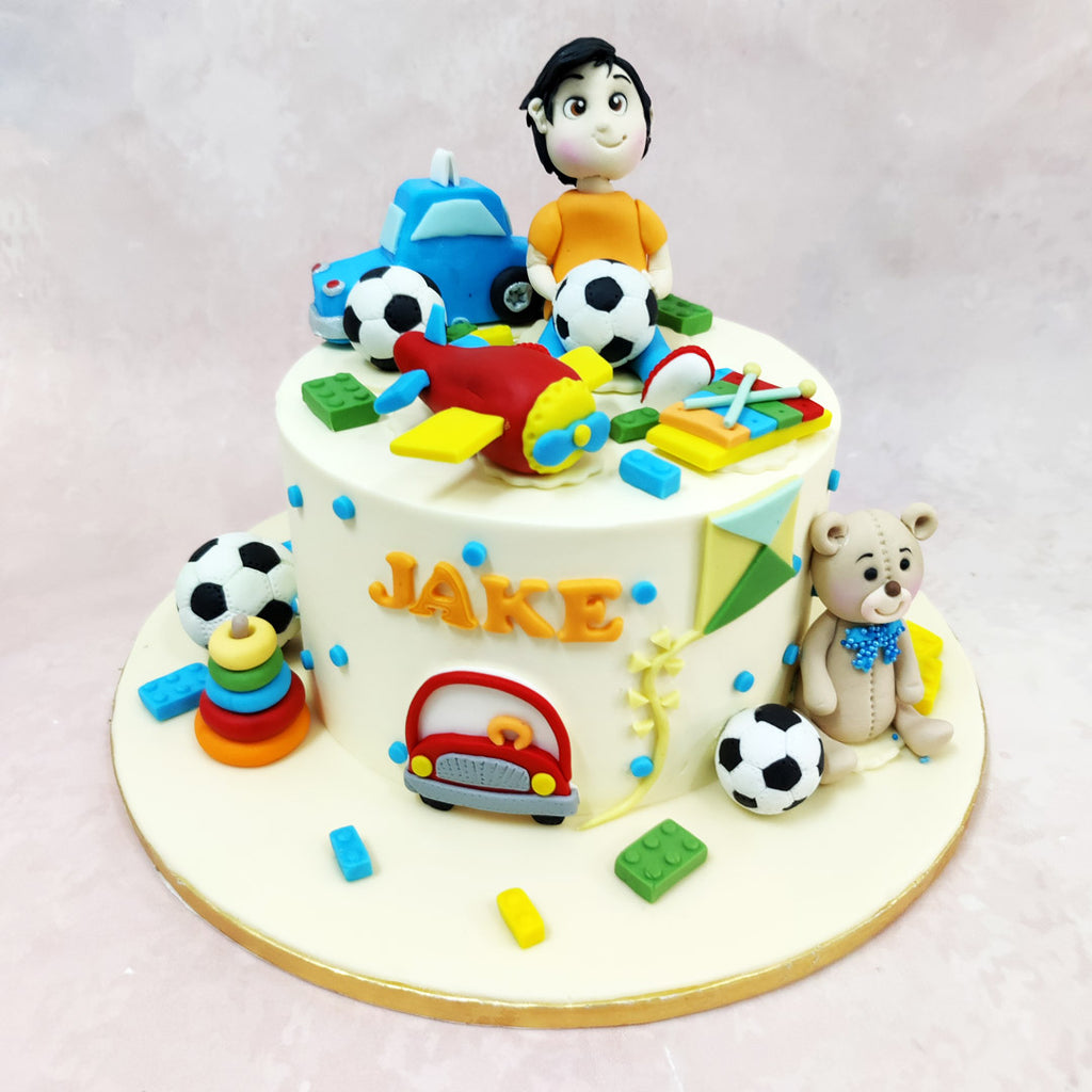 The design showcases an enchanting collection of handcrafted elements, from miniature football balls scattered playfully around this Birthday Cake For Kids to carefully modelled building blocks in cheerful primary colours that spark imagination and creativity.