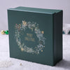 Green Christmas-themed gift box with wreath design and 'Merry Christmas' text on a snowy surface.