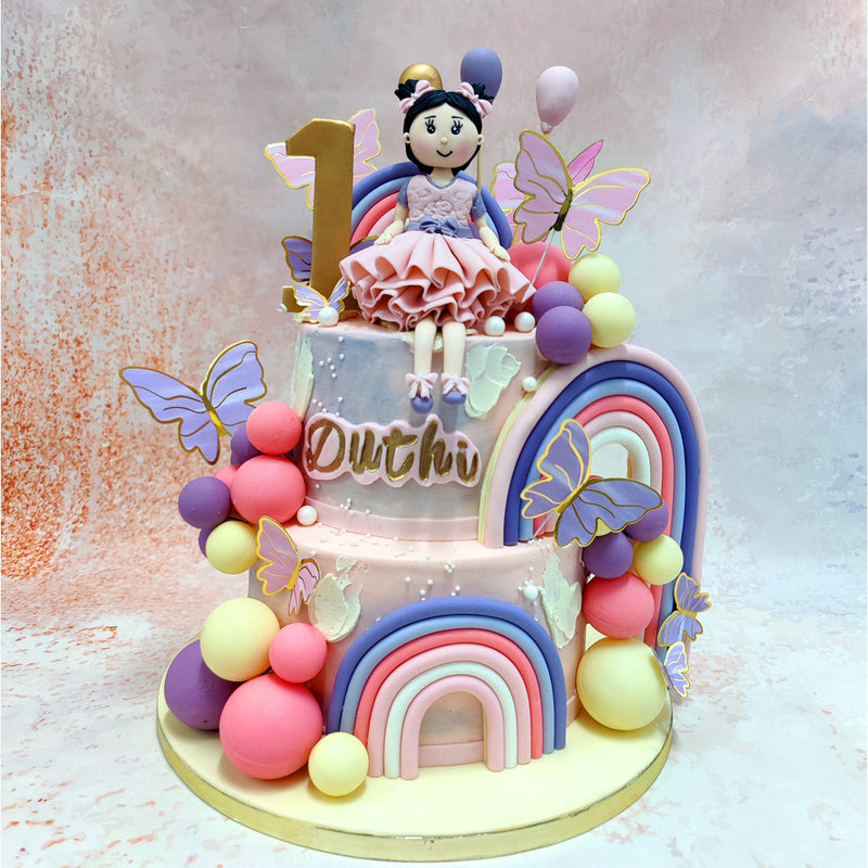 The design of this Princess Rainbow Cake radiates with soft pastel hues, from the elegant rainbows that arch gracefully on each tier to the delicate butterflies that seem to flutter with a life of their own. 