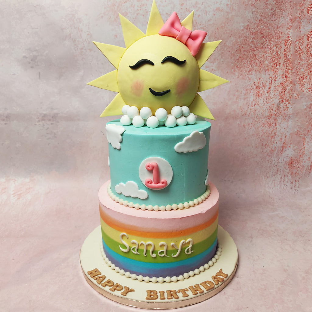 The bottom tier of this Sun Cake features a vibrant rainbow to pink ombre, embodying the joyful spectrum of childhood.
