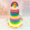 The upper tier of this Rainbow Buttercream Cake boasts an impressive display of meticulously crafted ruffle work, with each layer transitioning seamlessly through the colours of the rainbow - from delicate pink through to vibrant yellow