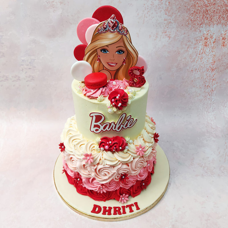Perched atop this fashion-forward Rosette Barbie Cake is Barbie herself, her blonde locks and mesmerising blue eyes captivating all who behold her presence.