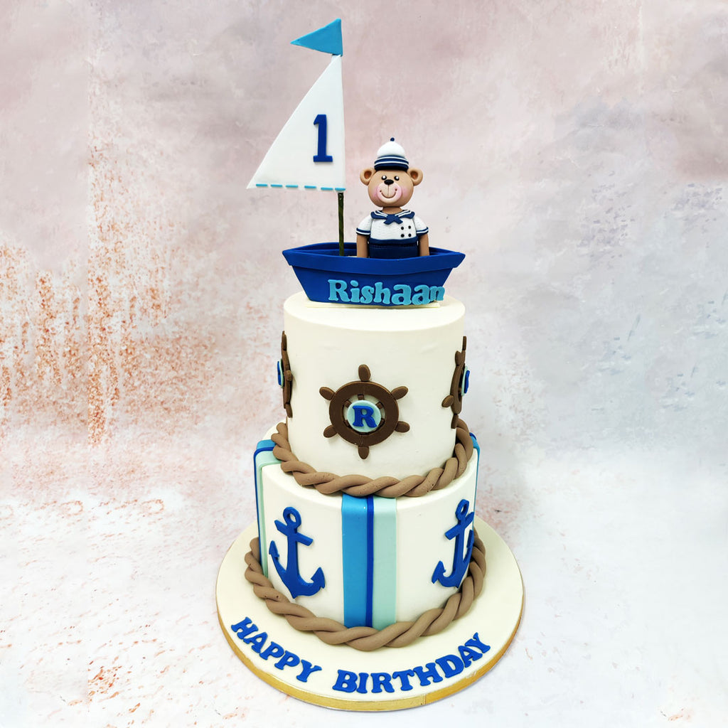 This Sailor teddy bear Cake showcases a charming blue sailboat, complete with a triangular white sail, captained by an adorable edible bear dressed in a sailor’s uniform.