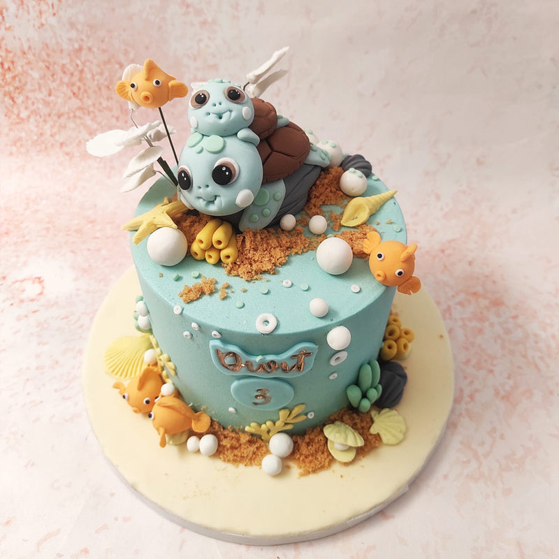 This charming Sea Life Cake features a delightful scene of sea creatures, including an adorable turtle with its baby perched atop, surrounded by vibrant coral reefs and playful fish. 