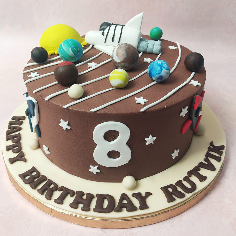 On a rich brown base, the universe comes to life on this Planet Cake design, adorned with twinkling white stars and a celestial array of planets, including our very own sun.