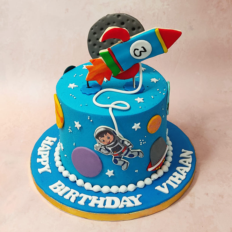 The astronaut on this galaxy themed cake is created in the likeness of an action figure and can be seen orbiting through the planets,  strung to a rocket figurine shooting out of the top with a realistic moon figurine behind it. 