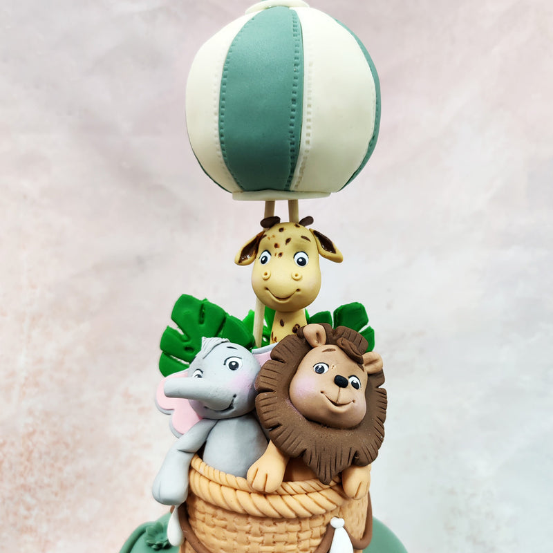 The middle tier of this Storybook Cake features a mischievous monkey swinging through with characteristic charm, surrounded by delicate sage-green foliage.