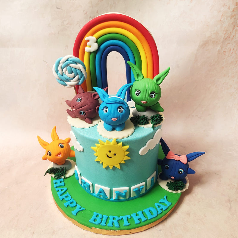 Start at the bottom of this Sunny Bunnies Cake, where alphabet blocks playfully spell out the name of the birthday star, mirroring the cheeky surprises that Sunny Bunnies are known for.   A vibrant rainbow appears on top of this Sunny Bunnies Birthday Cake, complemented by a knotted blue and white lollipop.