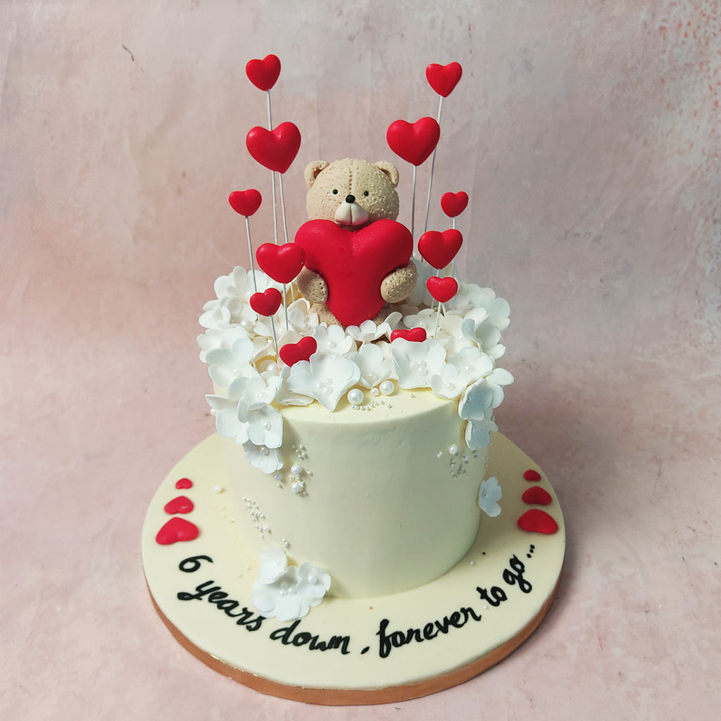 The tall off-white base becomes a canvas adorned with delicate edible white flowers, symbolising the blossoming journey you've shared through this Teddy Anniversary Cake 