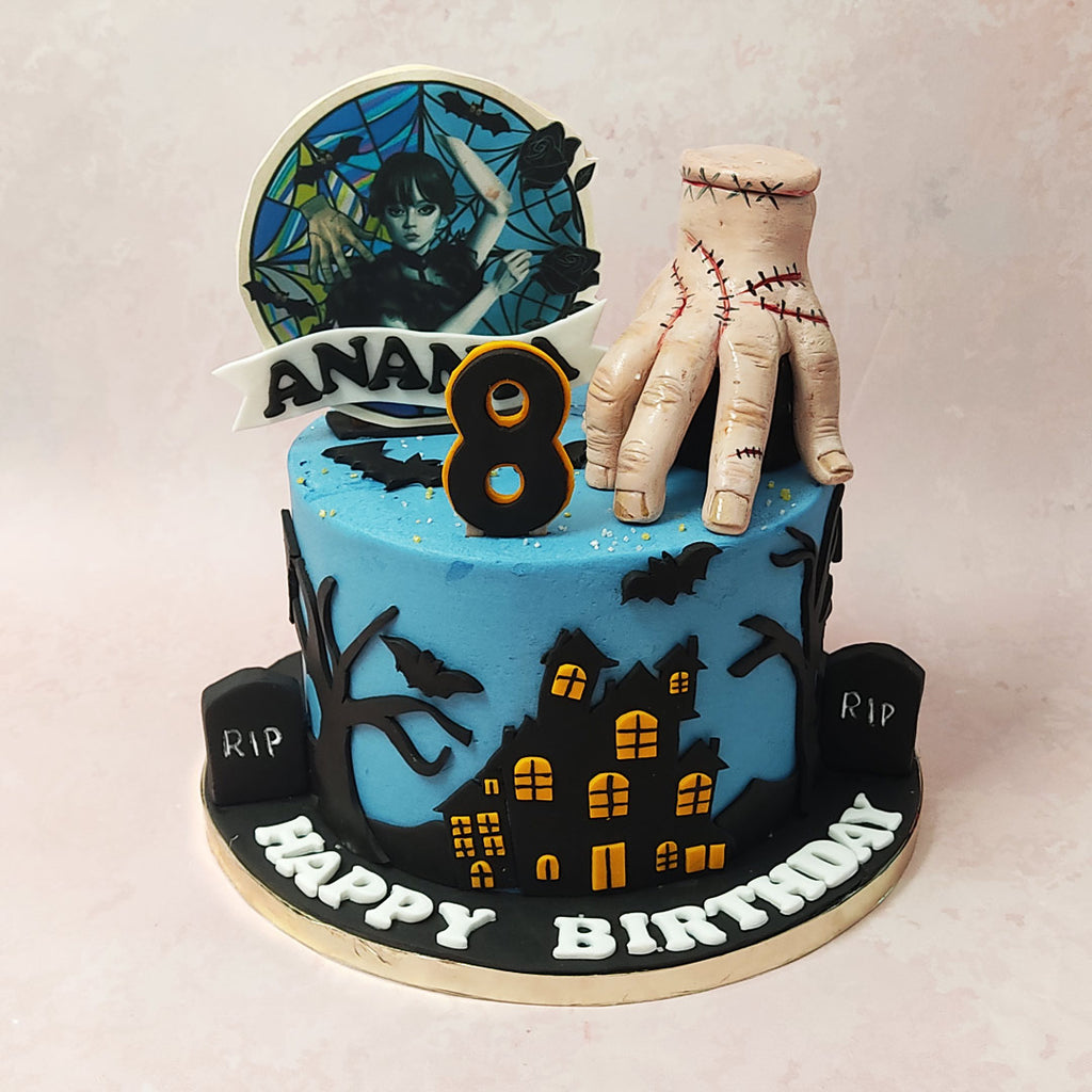 A Thing cake design with a blue base embellished in eerie silhouettes of tombstones, trees, houses with the window lights on and bats in a shade as black as black can be (much like what Wednesday usually adorns herself in), this Wednesday Addams cake is embedded with a variety of symbols from the show that'll have fans spooked in the best way possible.