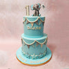 This whimsical blue elephant cake features a miniature figurine of an adorable blue elephant perched on the top tier, holding a flag in its trunk. 
