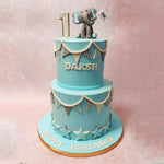 This whimsical blue elephant cake features a miniature figurine of an adorable blue elephant perched on the top tier, holding a flag in its trunk. 