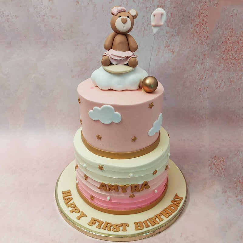 The bottom tier of this two tier teddy bear cake features a mesmerizing yellow to pink ombre buttercream frosting, reminiscent of a radiant sunrise. 