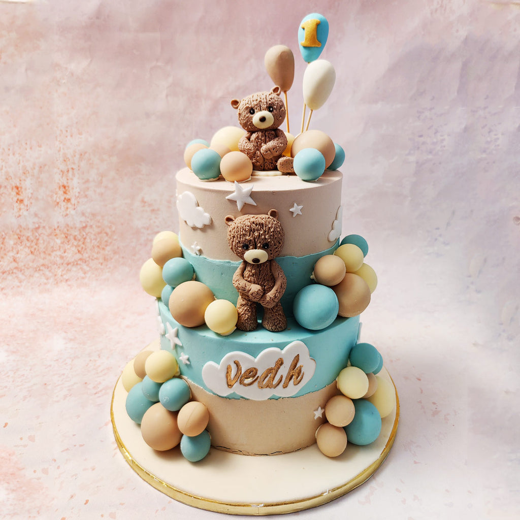 This Two Tier Teddy Bear Cake features a delightful blend of beige and blue hues, evoking a sense of calm and joy. 