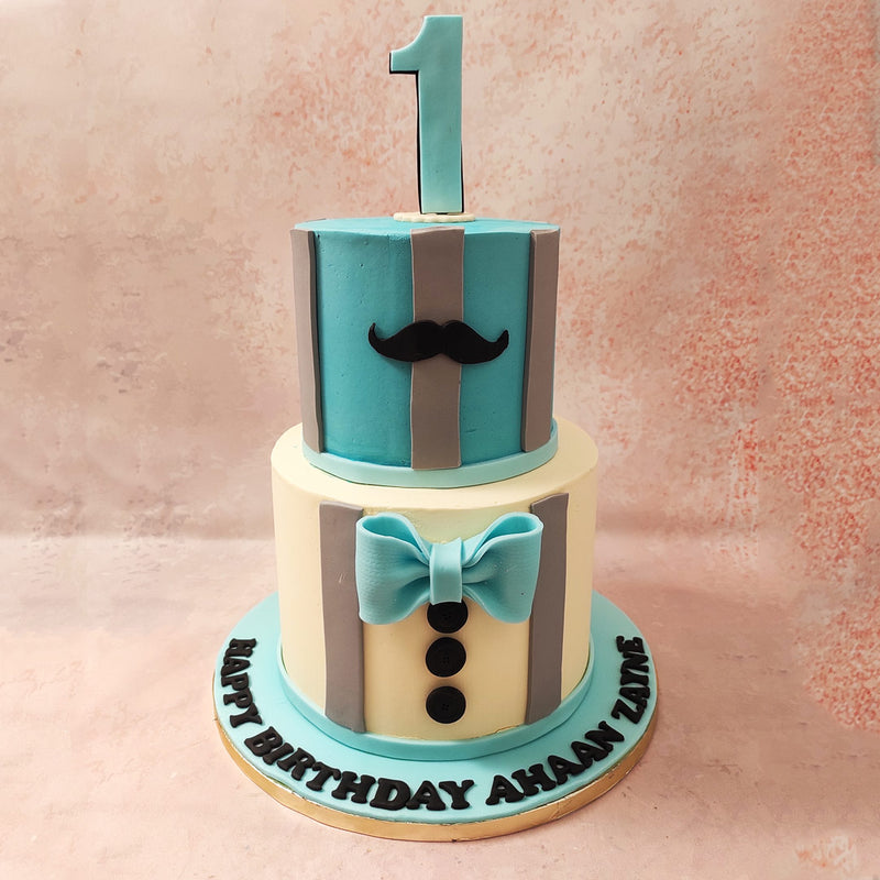The top tier of this two tier tuxedo cake boasts a blue hue and is adorned with a black moustache that adds a dash of humour and sophistication to it. 