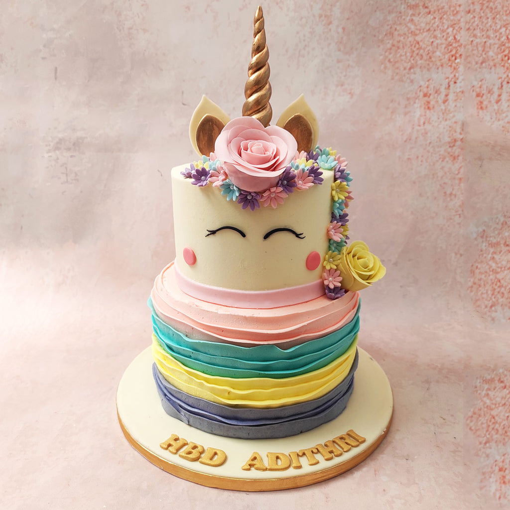 The bottom tie of this two tier Unicorn Face Cake, a kaleidoscope of colour, boasts a concentric and colourful buttercream piping.