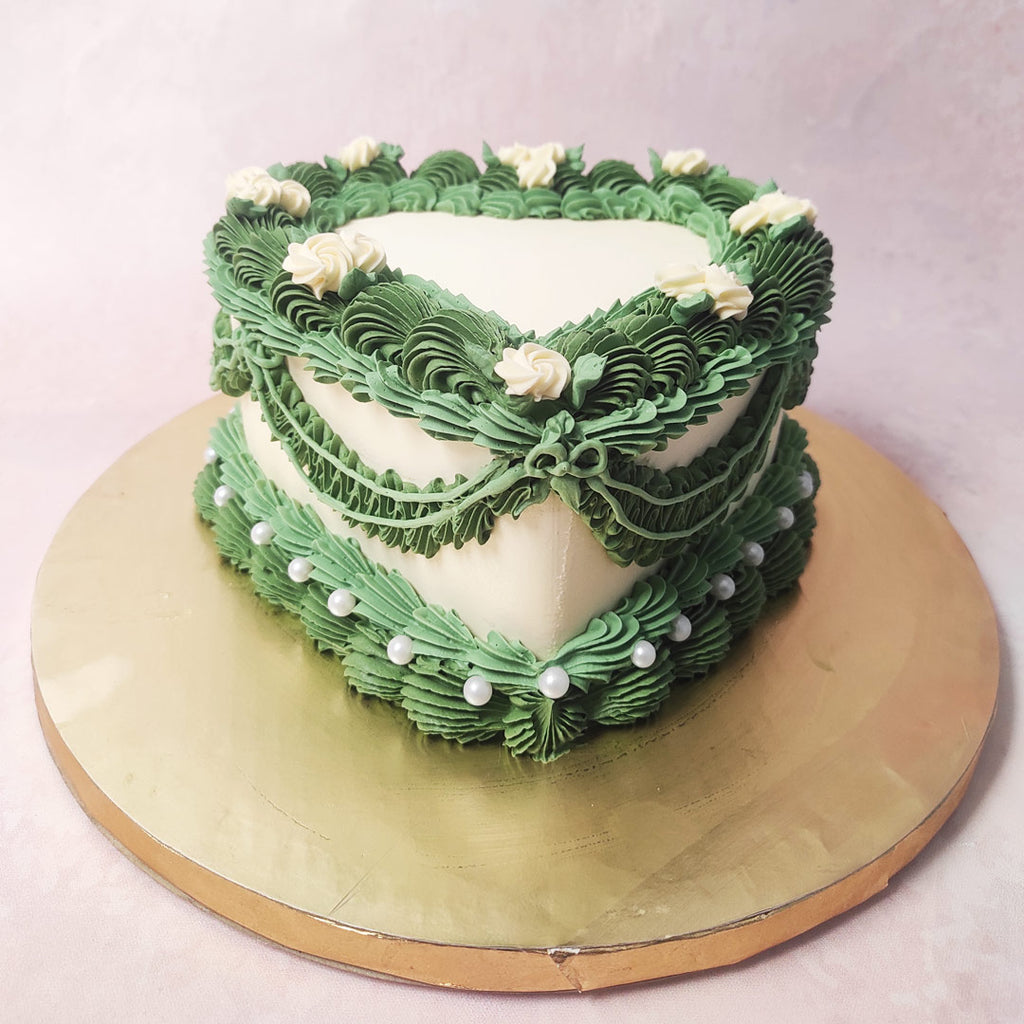 Adorned with intricate layers of lush green buttercream piping, meticulously crafted to resemble a delicate floral wreath, this Green Heart Cake exudes a charming vintage allure.