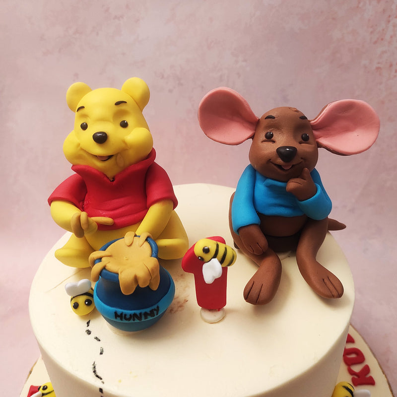 The presence of Winnie the Pooh, his pot of honey, and Roo the young kangaroo brings to life the magical world of Hundred Acre Wood on this Winnie The Pooh Theme cake. 