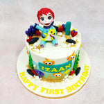 Sitting right at the top of this Yellow Baby Shark Cake is an adorable fondant figure of Bebefinn, clutching his cheerful yellow shark pal and beaming with first-birthday wonder. His wide eyes and tiny paws give the whole piece a playful, animated charm—as if he’s just paused mid-dance from a deep-sea singalong.