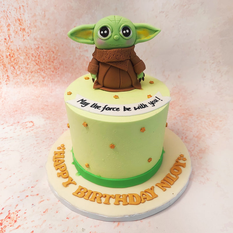 The smooth green base of this Yoda Cake is delicately adorned with small golden stars, creating a celestial backdrop that captures the wonder and mystery of the Star Wars universe. 