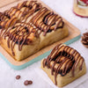 Individual chocolate sweet roll and a platter of rolls with rich chocolate ganache drizzle, served on a wooden board.