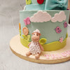 Like the perfect picture of a safe and beautiful nursery, this first birthday cake design also features a variety of pretty ornaments in light pastel colours as wreaths of flowers, bows: a big blue one draping the bottom of the top tier and a small green hill draping the bottom of the bottom tier  