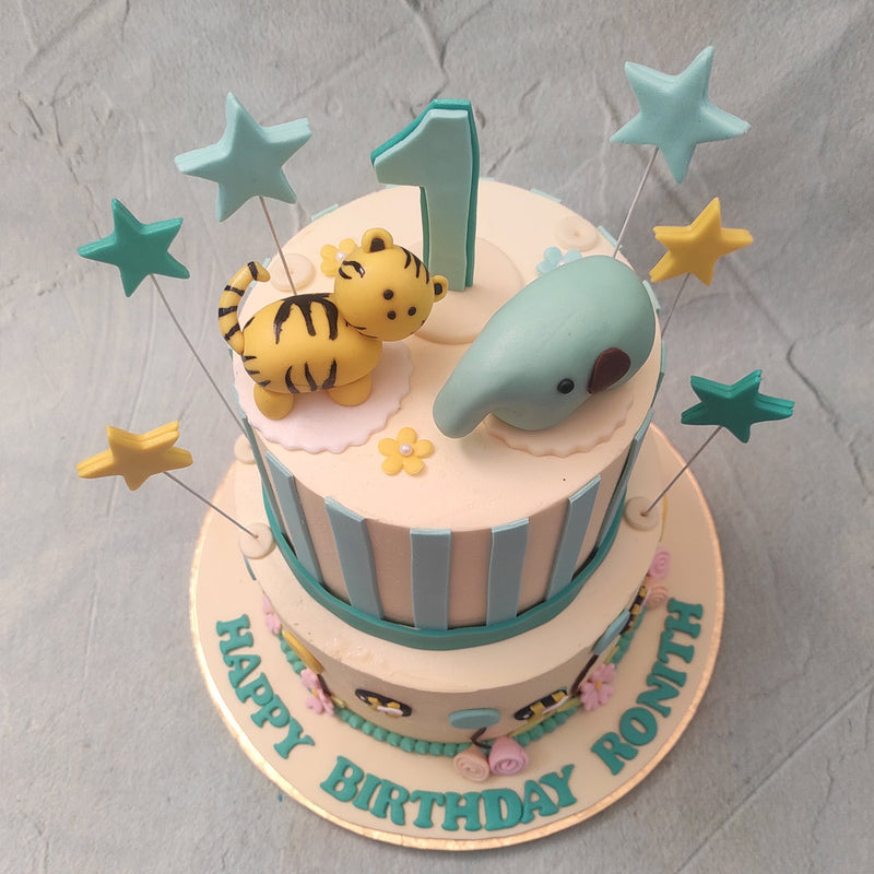 At the base of the bottom tier is a string of edible, green beads wrapped around this animal theme 1st birthday cake for kids with pink and peach buttercream flowers forming the charm on this ornamental bracelet.