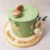 Edible gold leaves adorn the side, complemented by buttercream pipings and on top of this macaron cake design rests two beautiful, gold sumptuous macarons presented as if this piece is a dessert platter. 