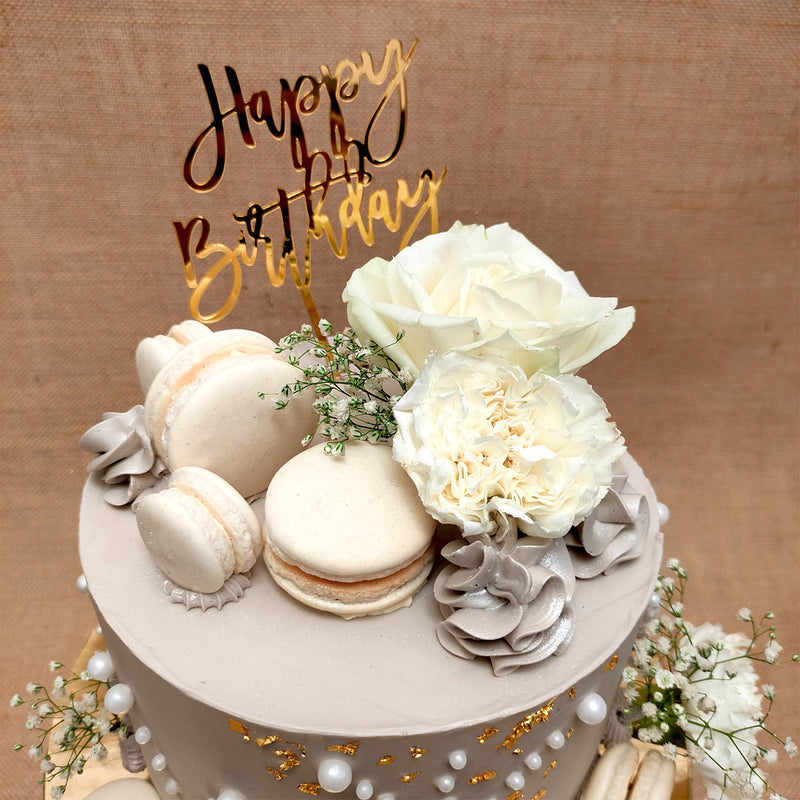 Top view of our beautiful birthday cake for wife or you can say florist cake because it holds lot of edible flowers which are hand made and along with it there are tasty macaroons as well and a happy birthday golden topper