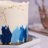 Here we have a white base with different shades of blue forming the ornamentation at the bottom of this special cake. The uneven coating of frosting on top of this blue cake design complements the decorations at the bottom.