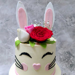 The bunny cake topper is its two ears that stand straight up in all its edible glory in between which is a carefully placed bouquet of flowers to add to both the elegant aesthetic and the placement of the bunny cake design in and around elements of nature.