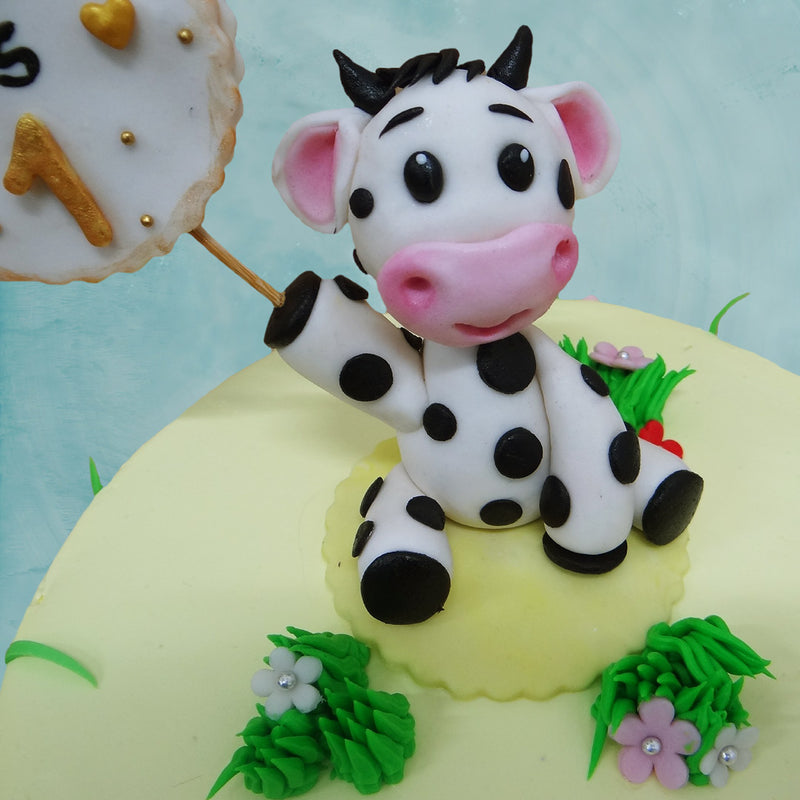Zoomed view of cow themed birthday cake where a baby cow is holding a stick with a cute message for your little one. This cow cake will surely be loved by your little one