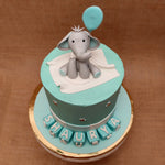 Top view of elephant baby shower cake where a cute baby elephant is looking straight at you while holding a blue balloon. This cute elephant cake is the best way to celebrate your kids first day