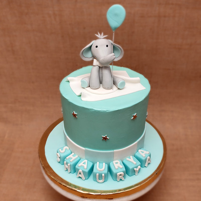 Elephant theme baby shower cake with a cute small baby elephant on top of the cake looking straight at you while holding a blue balloon. This cute elephant cake is prefect as a baby shower cake
