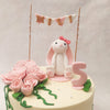 This floral bunny cake design also features a tiny wooden arbor with pink and white banner flags on it that perfectly match the colour palette. 