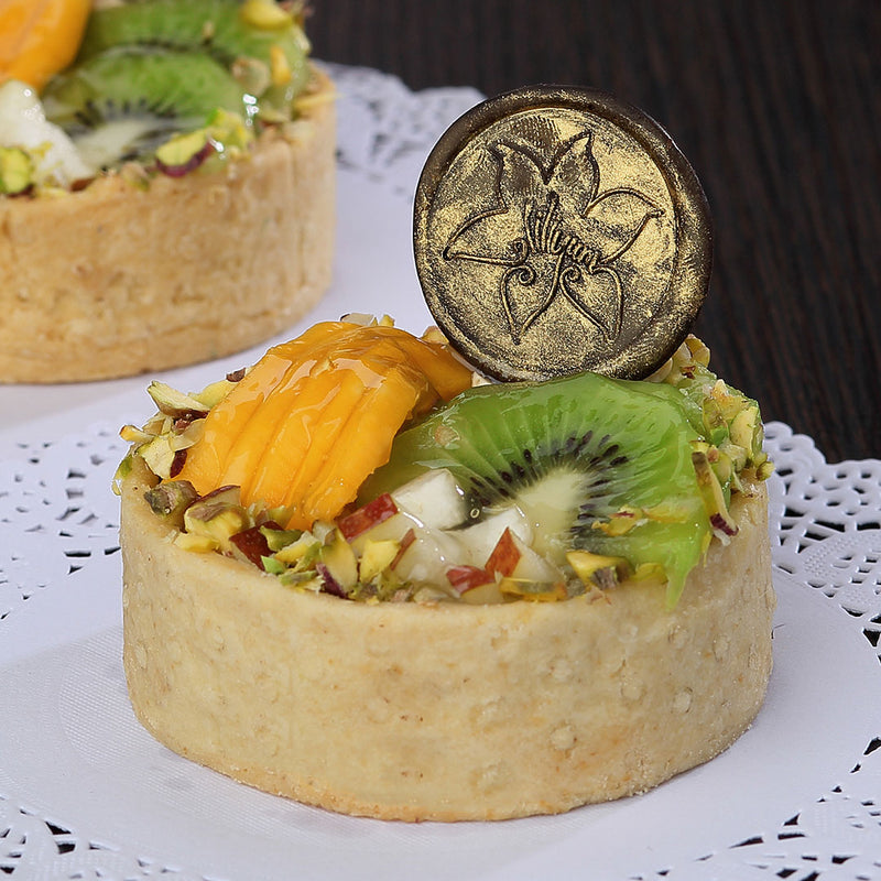 Zoomed view of fresh fruit tarts with real fruits on top and a cute liliyum logo on chocolate disk engraved