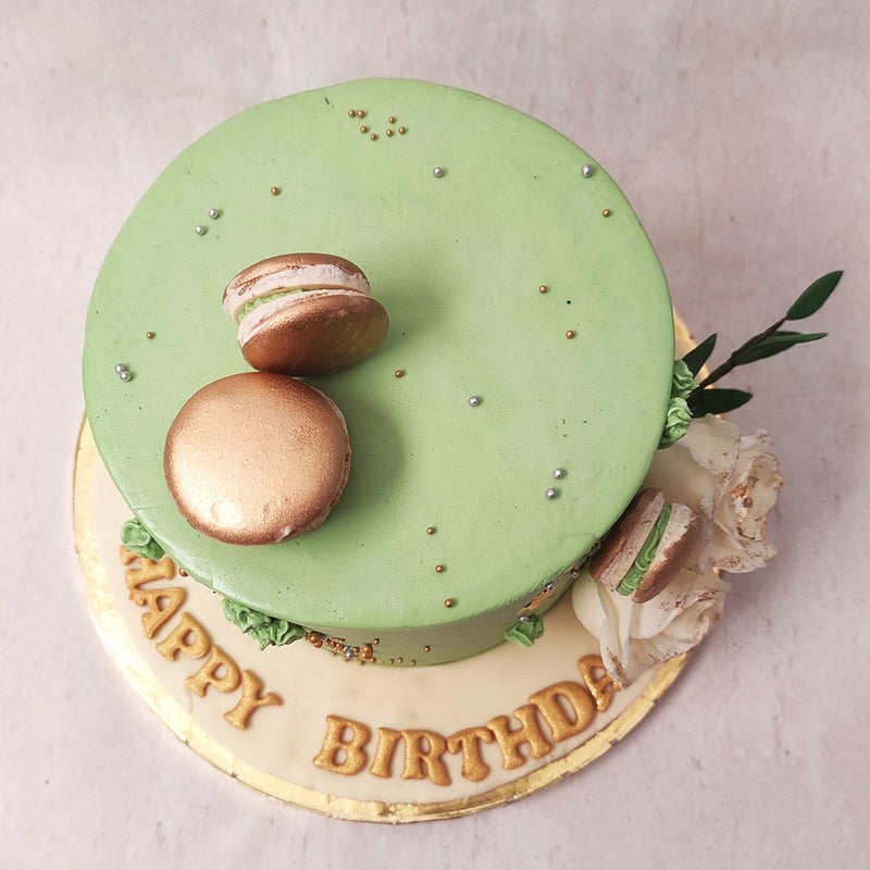 Fresh white roses are embedded into the side of this green floral cake with macarons adding to the naturesque theme of this piece.