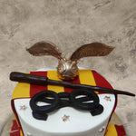 Zoomed view of harry potter birthday cake to show you the main elements on this cake like magic wand, harry potter glasses, golden snitch and a gryffindor house colored scarf