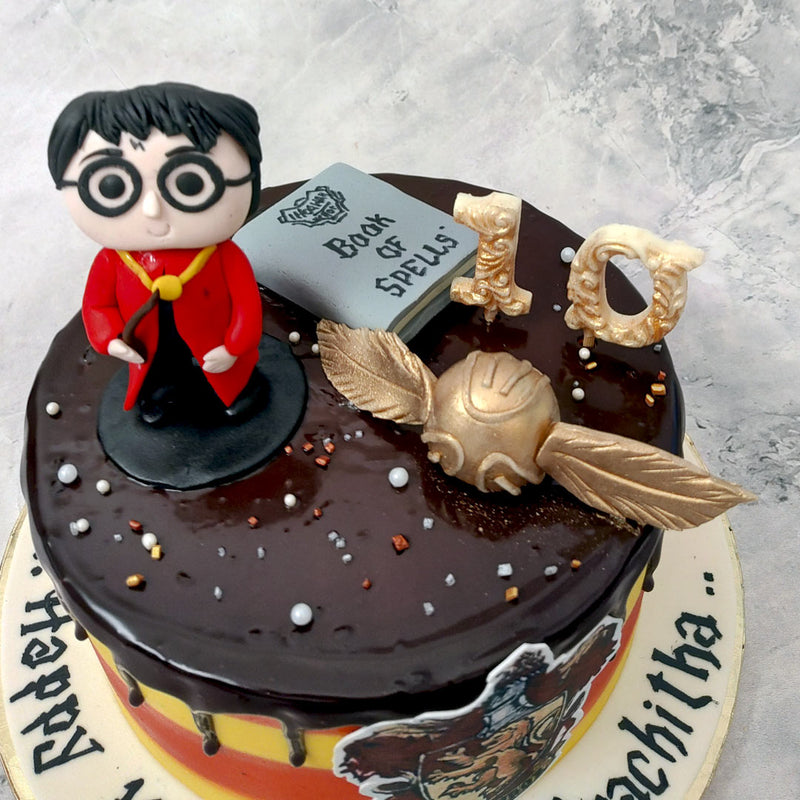 A toy figurine of Harry himself stands proudly on top in the red cape he wears for quidditch matches, waving his wand and casting some special magic on this Harry Potter drip cake for her/him